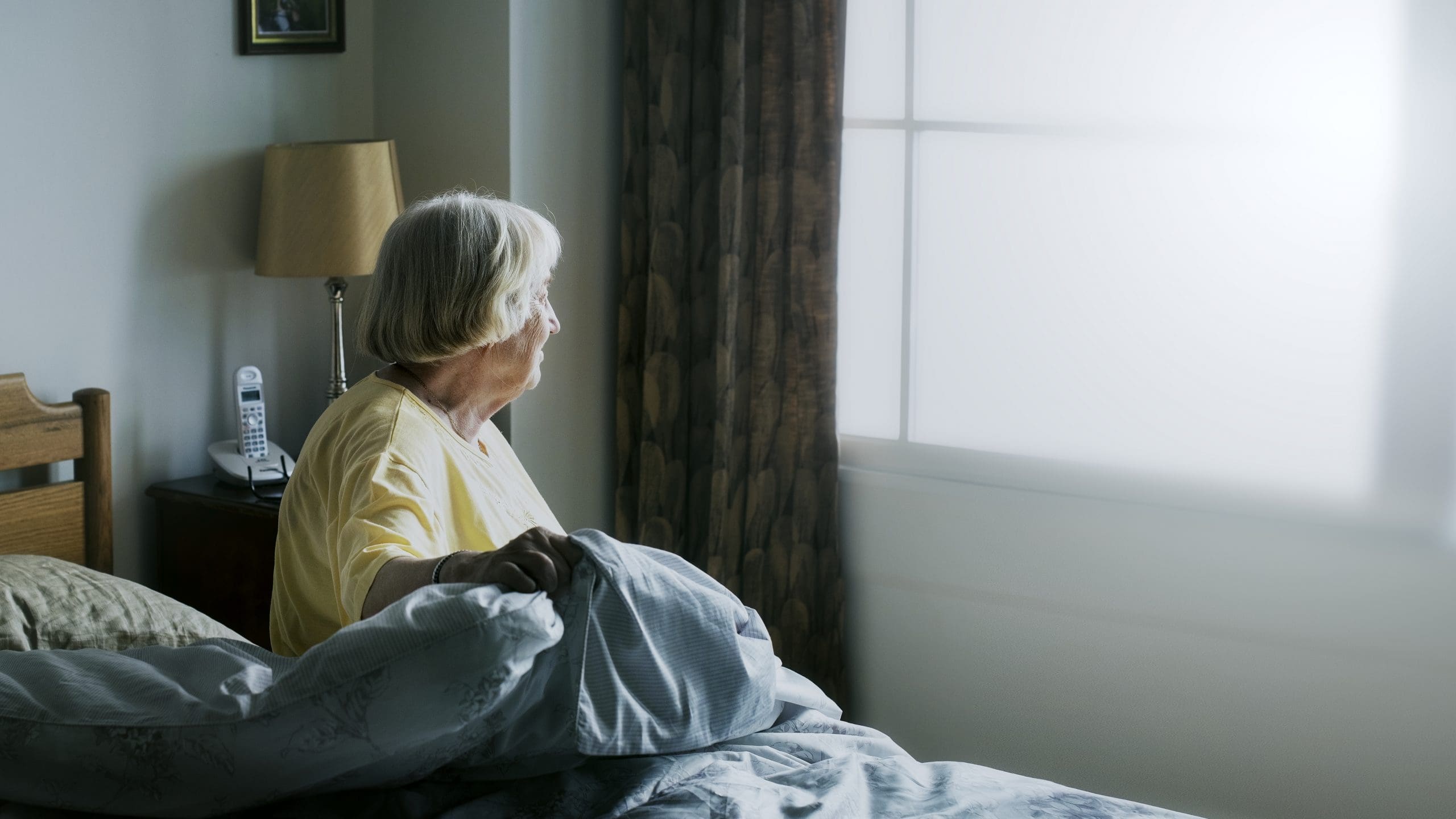 Senior woman sitting in a bedroom looking out of her window
