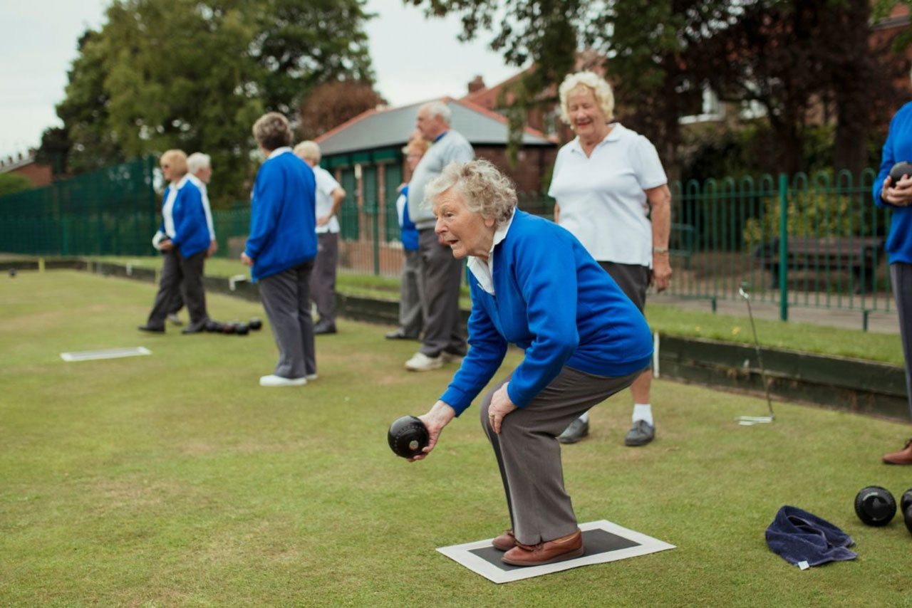 An older woman bending down to roll a lawn bowl