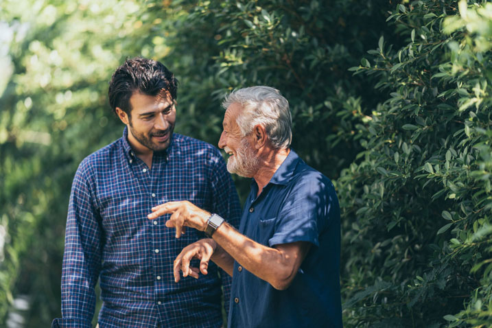 An older man happily talking with his adult grandson outside