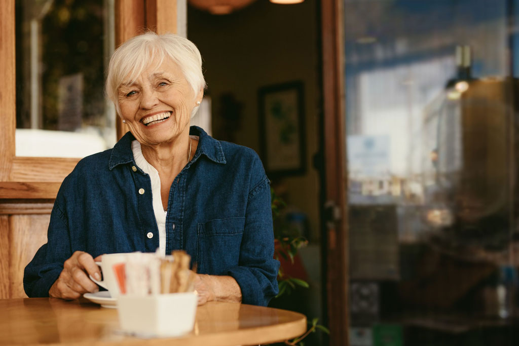 An older woman happily drinking coffee at a cafe