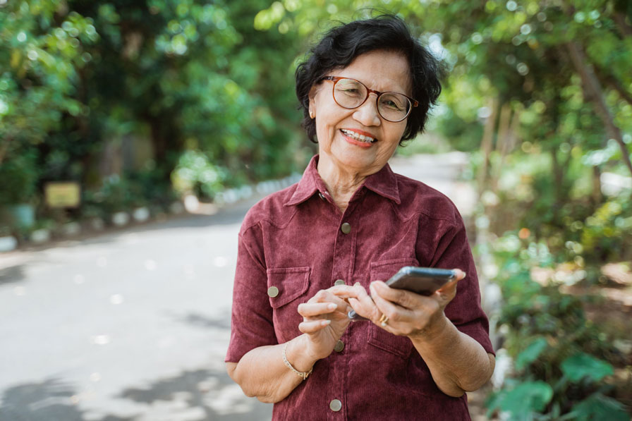 An older woman happily typing on her mobile phone while standing outside